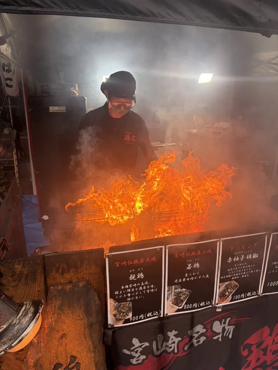炎が上がる焼き場で親鶏と若鶏を焼く鶏道のスタッフと、店頭の値札